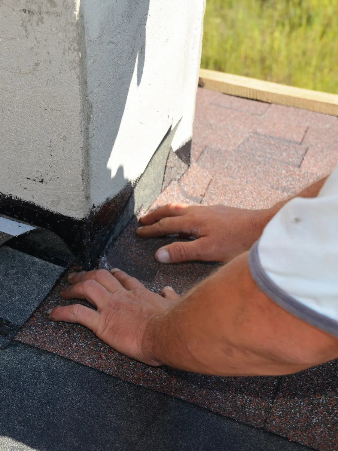 Hands pressing new flashing material into place where a chimney meets the roof